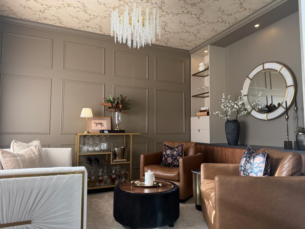 Elegant lounge with panelled walls, crystal chandelier, and cognac leather seating styled by Sherrie Funk Interiors